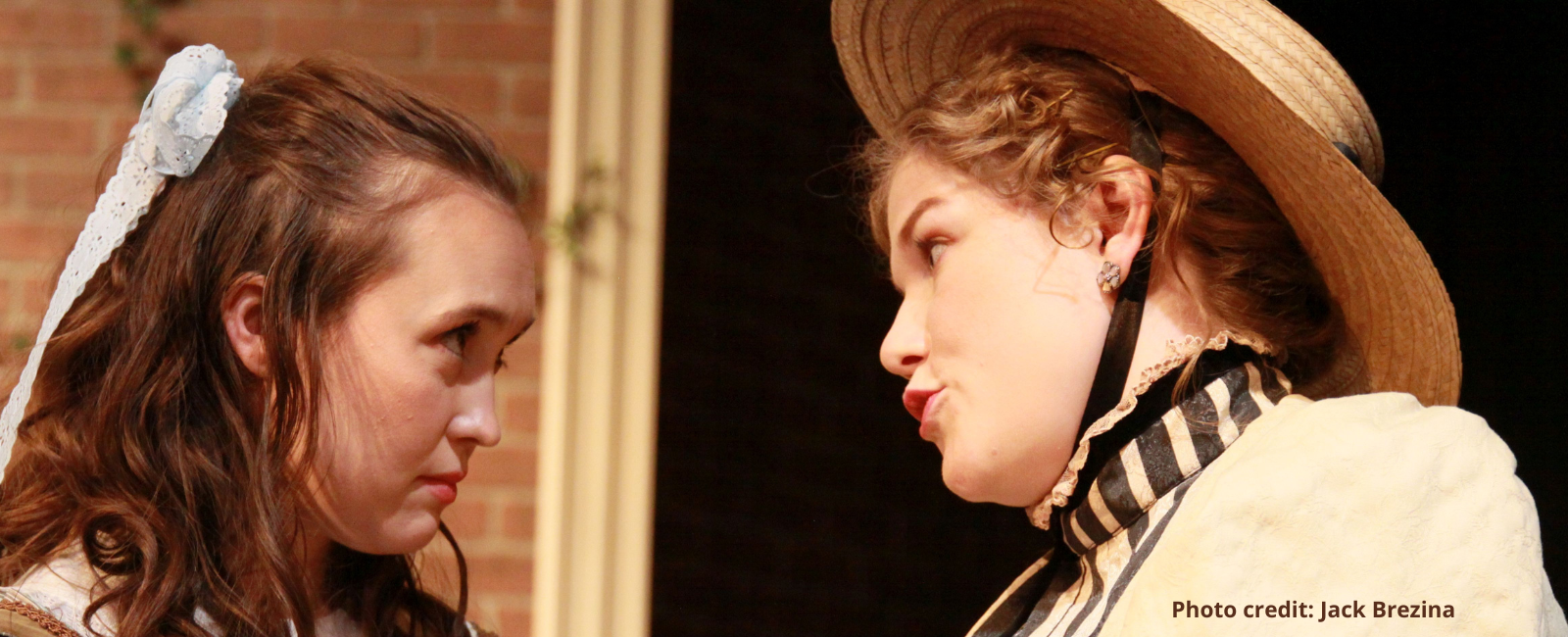 Two women facing each other, one with a broad hat on her head.